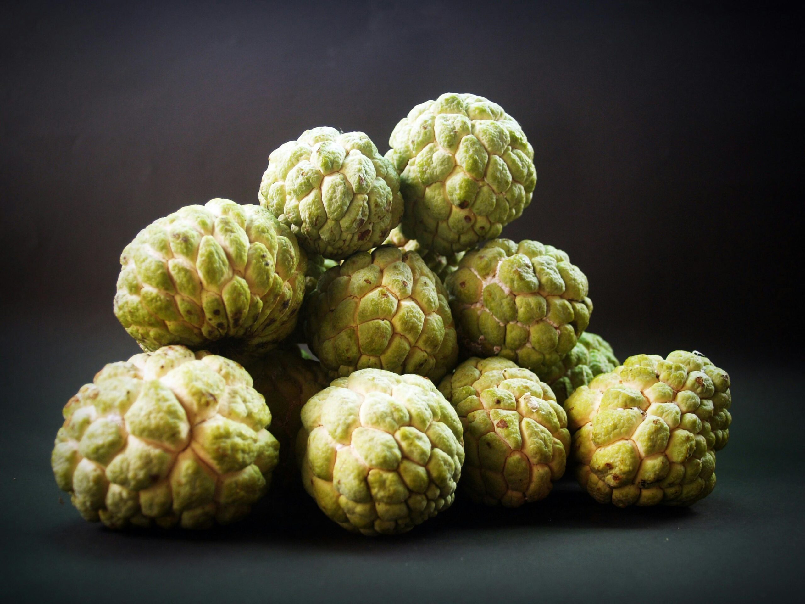 Bright green custard apples displayed against a dark background.